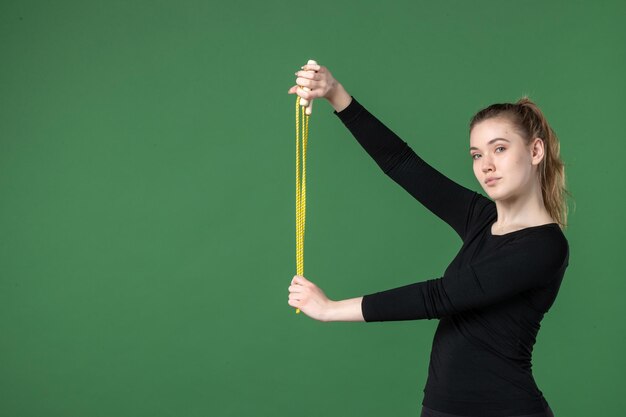 Mulher jovem segurando a corda de pular no fundo verde, vista frontal, esporte, atleta, ioga, saúde, corpo, mulher, ginástica