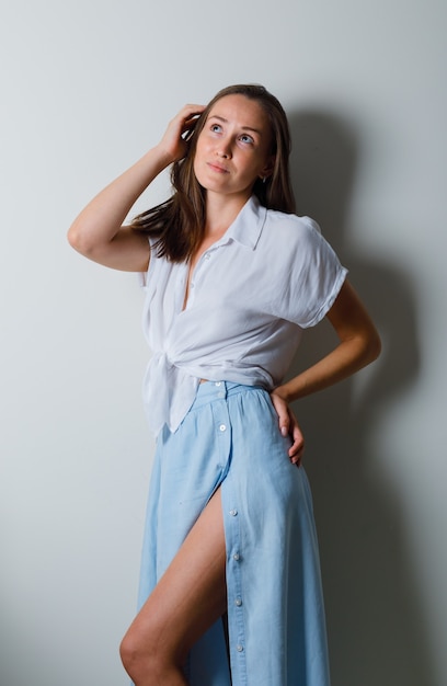 Foto grátis mulher jovem segurando a mão na cabeça e a outra mão na cintura em uma camiseta branca e saia azul claro e está linda