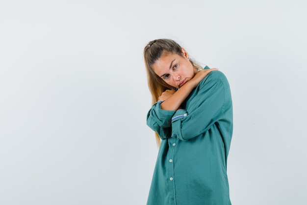 Mulher jovem segurando as mãos cruzadas nos ombros com uma camisa azul e parecendo cansada