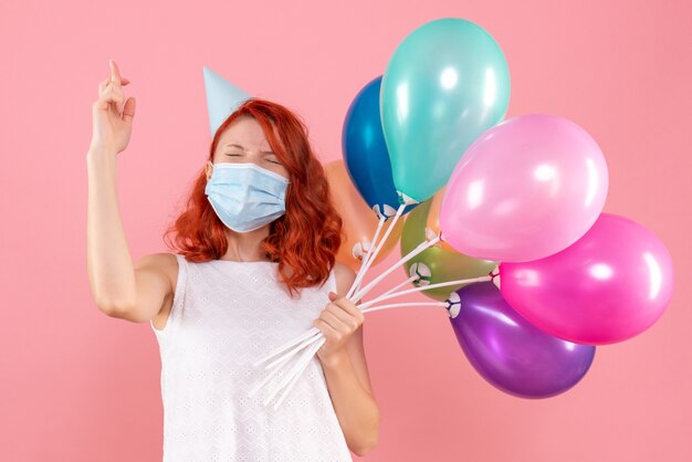 Mulher jovem segurando balões coloridos na máscara de frente para a festa de natal rosa vírus da cor da mesa