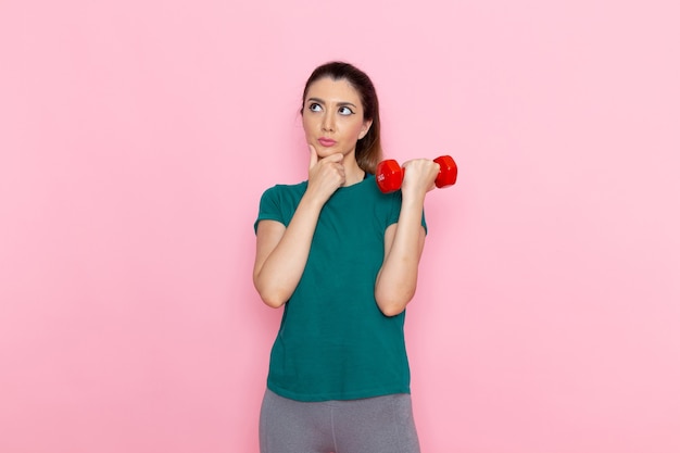 Mulher jovem segurando halteres na parede rosa atleta de frente para exercícios exercícios de saúde