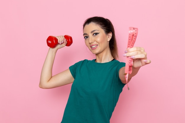 Mulher jovem segurando halteres vermelhos na parede rosa claro atleta de frente para exercícios exercícios de saúde