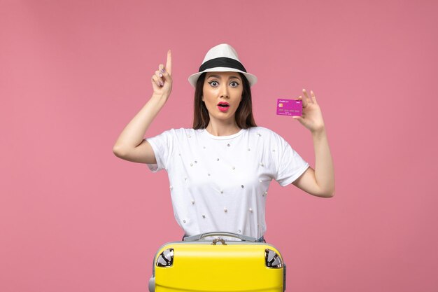 Mulher jovem segurando o cartão do banco em uma parede rosa claro férias dinheiro mulher de frente