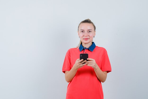 Mulher jovem segurando o celular em uma camiseta e parecendo alegre