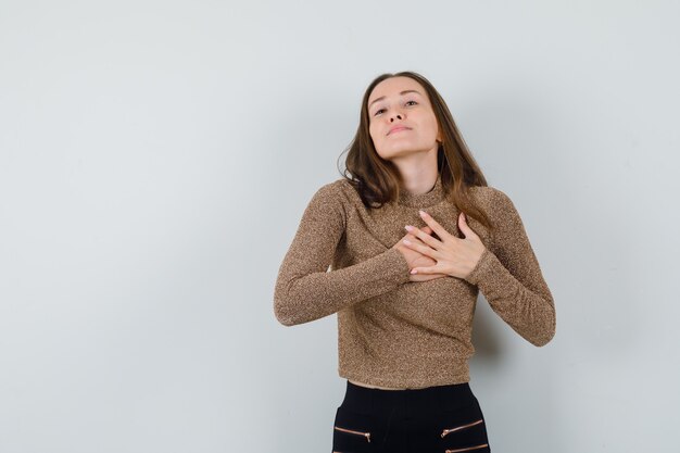 Mulher jovem segurando o coração com as mãos na blusa dourada e parecendo desejosa