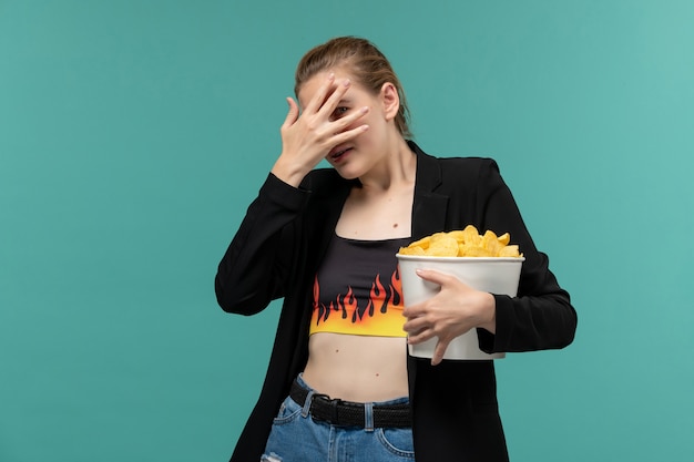 Foto grátis mulher jovem segurando o pacote com batata frita e assistindo filme na mesa azul