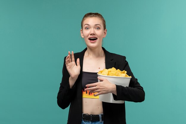 Mulher jovem segurando o pacote com batata frita e assistindo filme na superfície azul