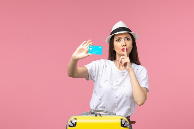 Mulher jovem segurando um cartão de banco azul na parede rosa mulher de frente, viagem de verão