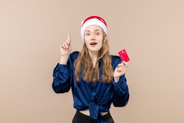 Mulher jovem segurando um cartão vermelho no fundo rosa. Foto do dinheiro do natal.