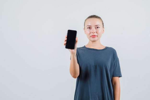 Mulher jovem segurando um telefone celular e sorrindo com uma camiseta cinza