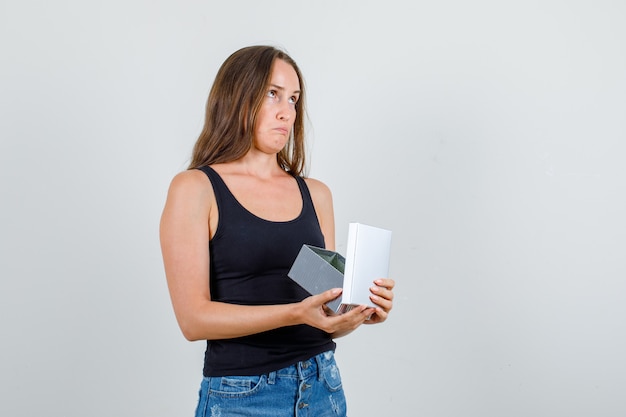 Mulher jovem segurando uma caixa de presente aberta em camiseta, shorts e parecendo confusa