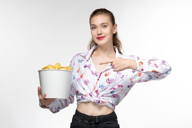 Foto grátis mulher jovem segurando uma cesta com batatas fritas de frente e assistindo filme com um sorriso na superfície branca