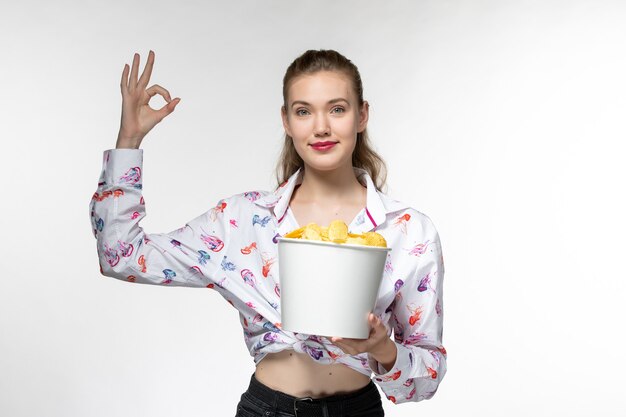 Mulher jovem segurando uma cesta com batatas fritas e sorrindo em uma superfície branca.