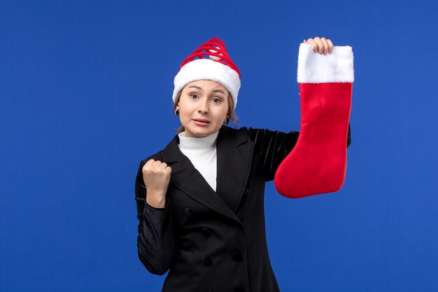 Mulher jovem segurando uma meia vermelha de Natal na mesa azul, feriado de ano novo humano
