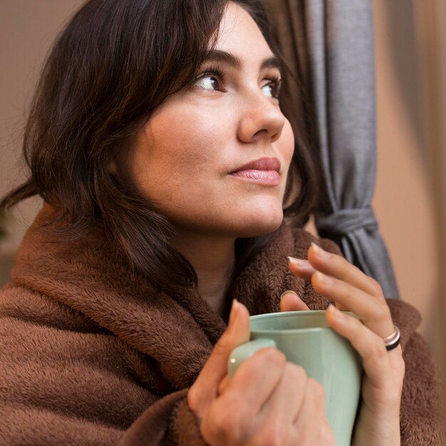 Mulher jovem segurando uma xícara de café enquanto é coberta por um cobertor