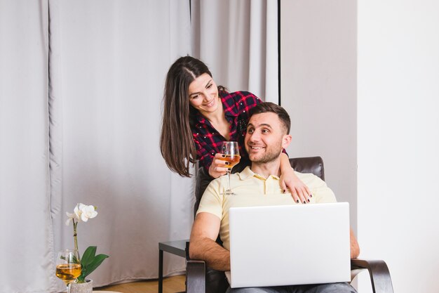 Mulher jovem, segurando, wineglass, estar, atrás de, a, homem, usando computador portátil