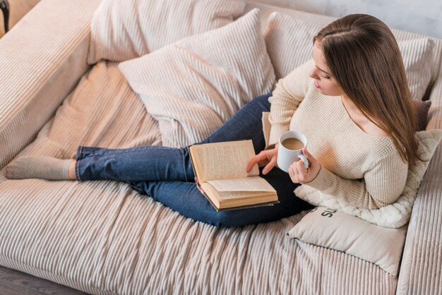 Mulher jovem, segurando, xícara café, leitura, livro