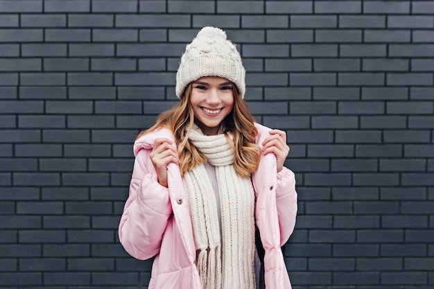 Mulher jovem sensual de bom humor, caminhando em um dia frio. Retrato ao ar livre de uma agradável menina loira posando com chapéu de malha.