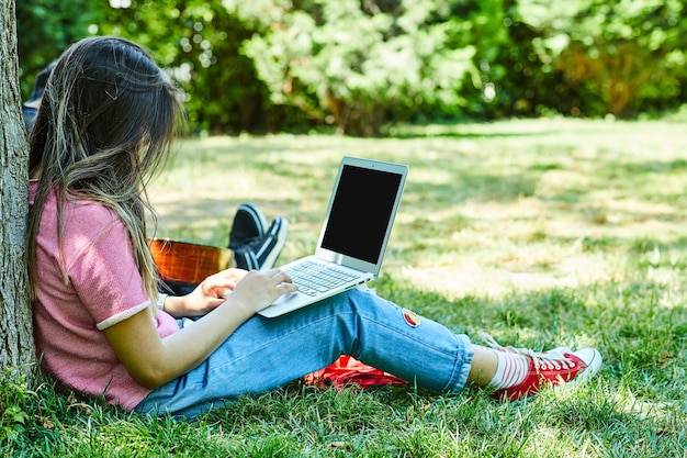 Mulher jovem sentada na grama verde enquanto usa o laptop