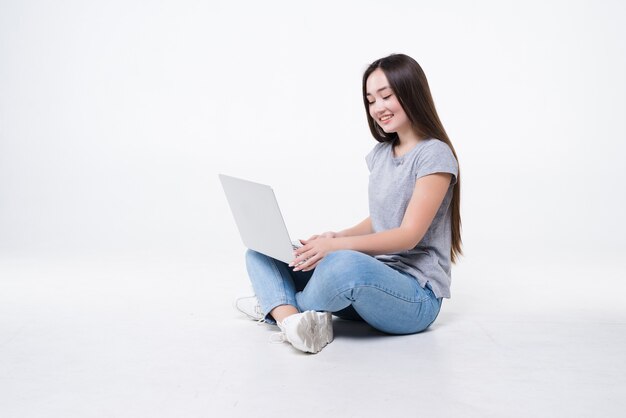 Mulher jovem sentada no chão com laptop isolado na parede branca