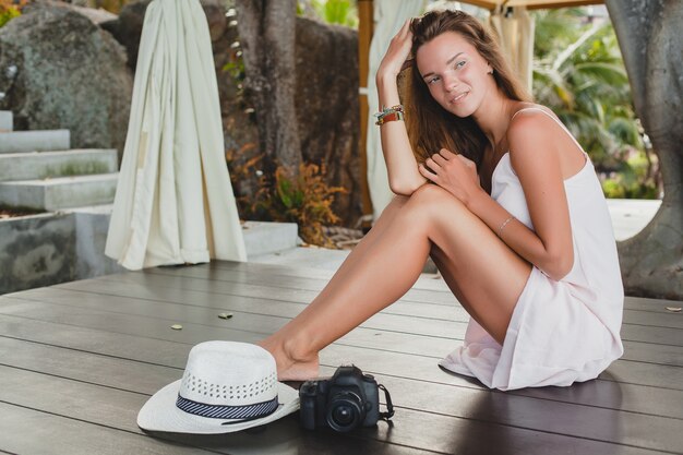 Mulher jovem sentada no chão com os pés descalços em um vestido claro, sorrindo