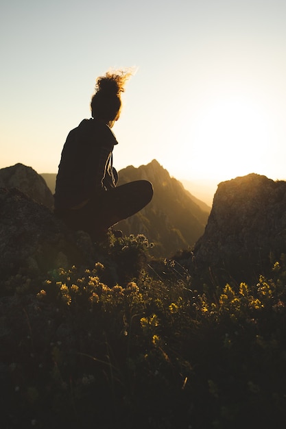 Mulher jovem sentada no topo da montanha apreciando a vista durante o pôr do sol