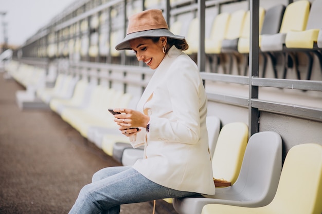 Mulher jovem sentada nos assentos da arena e falando ao telefone