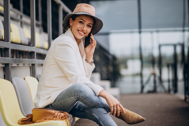 Mulher jovem sentada nos assentos da arena e falando ao telefone