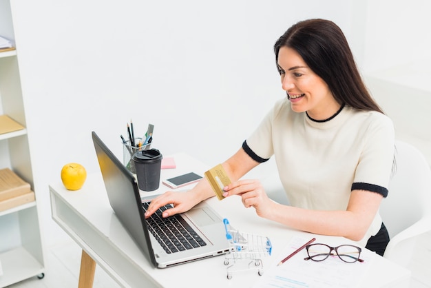 Mulher jovem, sentando, com, cartão crédito, em, tabela, com, laptop