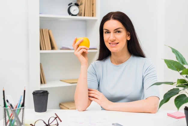 Mulher jovem, sentando, com, maçã, em, escritório