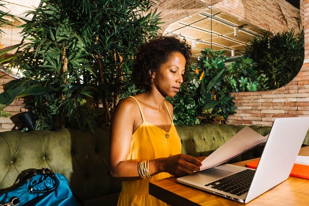 Mulher jovem, sentando, em, a, restaurante, leitura, documento, com, laptop, ligado, tabela madeira