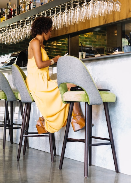 Mulher jovem, sentando, ligado, tamborete barra, usando, smartphone, em, a, restaurante