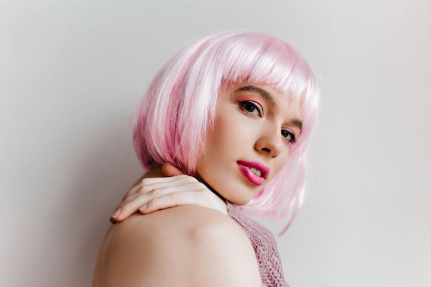 Mulher jovem sonhadora com maquiagem brilhante posando com prazer Foto de close-up da linda modelo feminina em peruca rosa olhando com um sorriso.