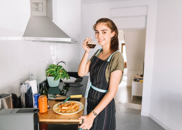 Mulher jovem sorridente bebendo café em pé no balcão da cozinha