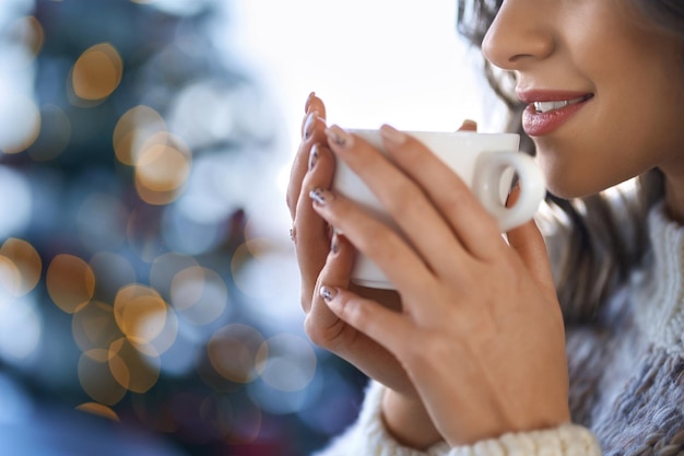 Mulher jovem sorridente bebendo chá ou café saboroso em casa