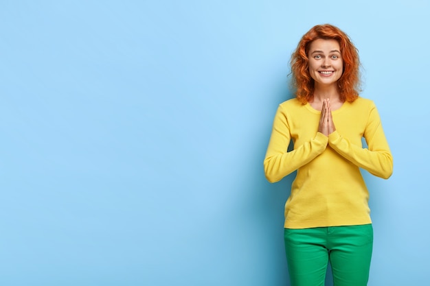 Foto grátis mulher jovem sorridente e calma revivida com cabelo ruivo ondulado, unindo as palmas