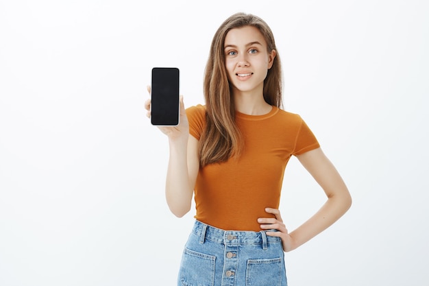 Mulher jovem sorridente e confiante dá conselhos, mostra a tela do smartphone, demonstra o aplicativo ou a loja