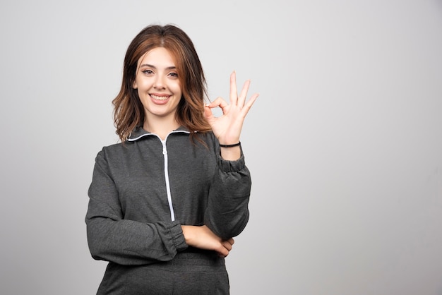 Mulher jovem sorridente em pé e mostrando gesticulando sinal de ok com os dedos.