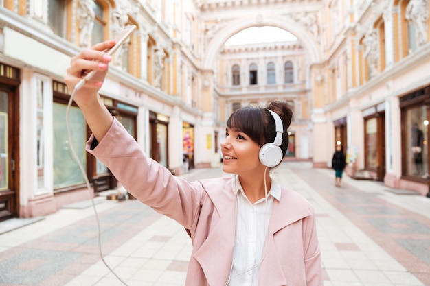 Mulher jovem sorridente feliz em fones de ouvido fazendo foto de selfie