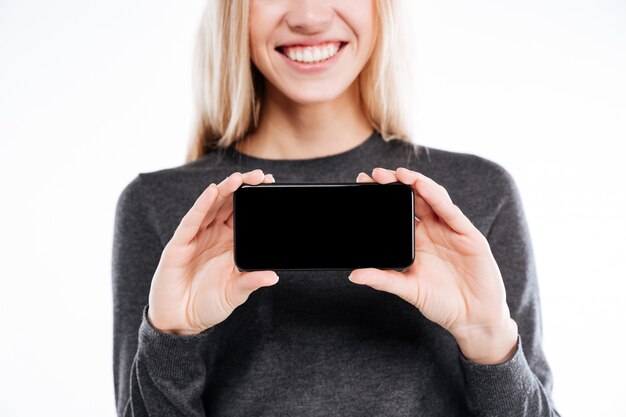 Mulher jovem sorridente, mostrando o telefone móvel de tela em branco para a câmera