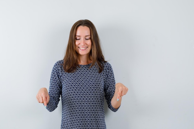 Mulher jovem sorridente mostrando para baixo com os dedos no fundo branco