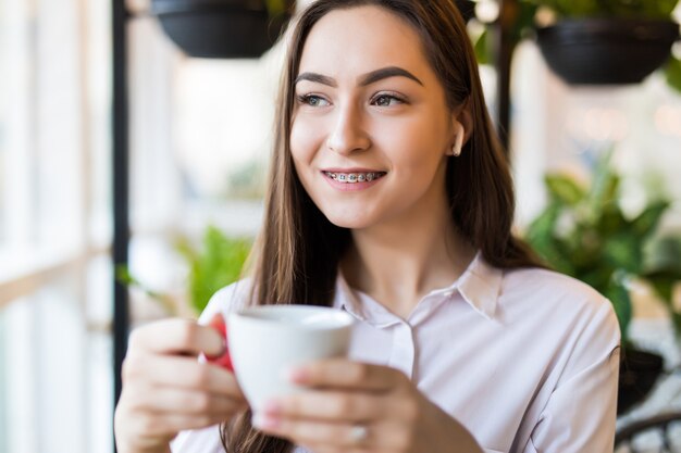 Mulher jovem sorridente no café com fones de ouvido, ouvindo música ou falando ao telefone