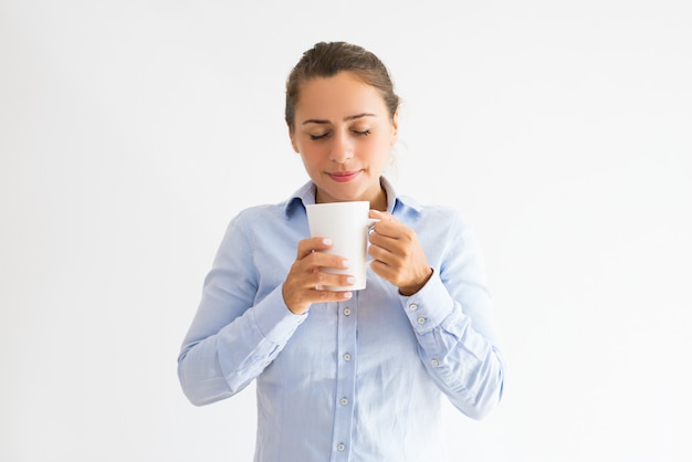 Mulher jovem sorridente segurando a caneca, cheirando e bebendo chá