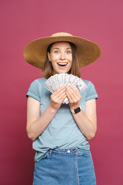 Mulher jovem sorridente segurando dinheiro na parede rosa