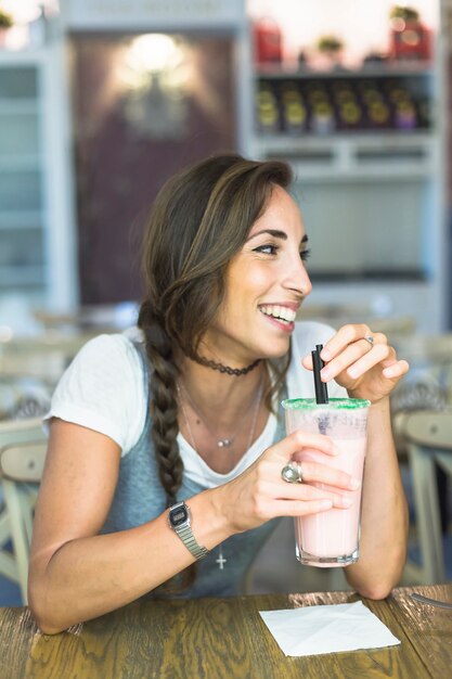 Mulher jovem sorridente segurando o copo de Milk-shake com lenço de papel na mesa
