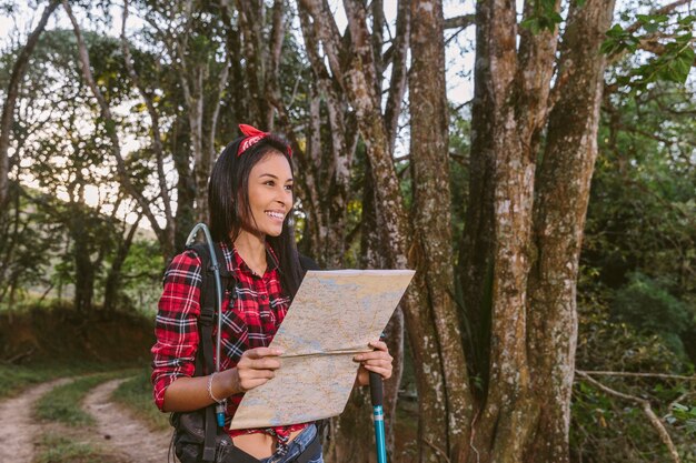 Mulher jovem sorridente segurando o mapa na floresta