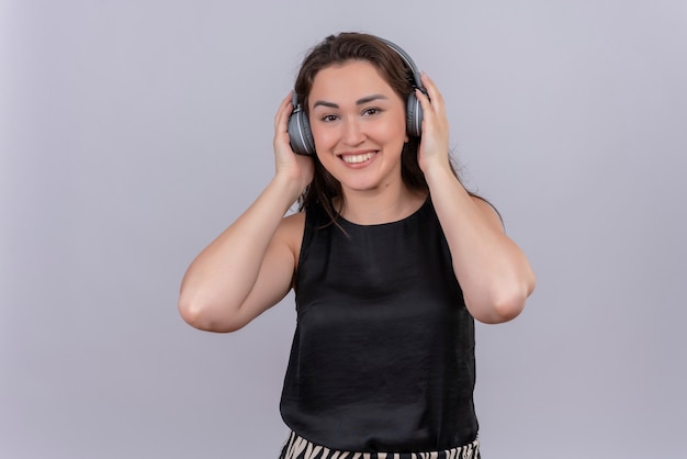 Mulher jovem sorridente usando camiseta preta em fones de ouvido na parede branca