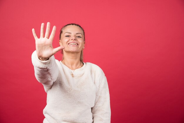 Mulher jovem sorrindo e mostrando o número cinco com os dedos