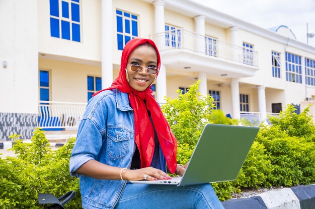 Mulher jovem sorrindo enquanto está sentada com seu laptop em um parque