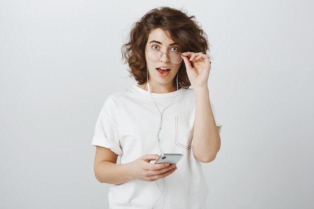 Foto grátis mulher jovem surpresa e interessada parecendo animada enquanto usa fones de ouvido e telefone celular